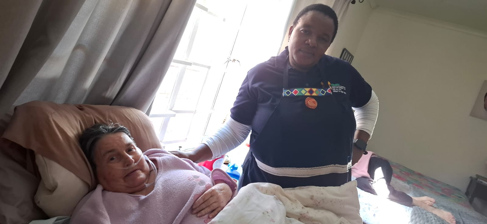 Caregiver standing beside a client resting comfortably at home