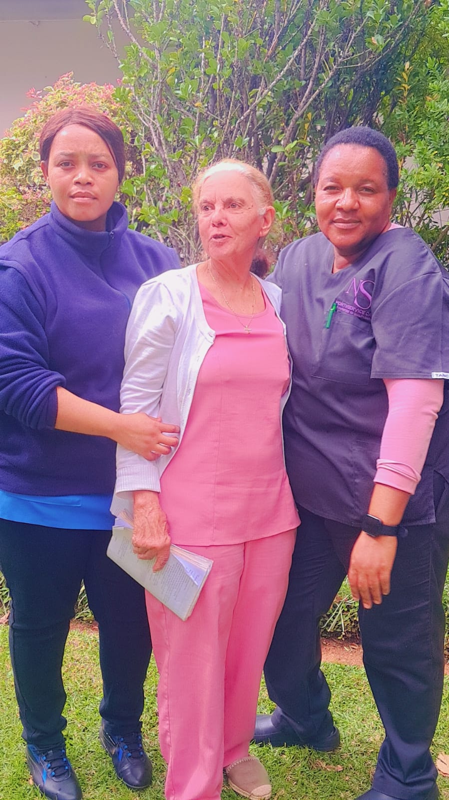 Two caregivers standing with a client in a garden